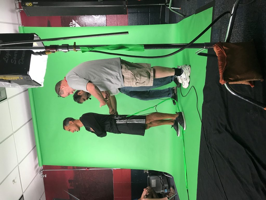 Crew setting up a full-length green screen with lighting and camera support during a studio production